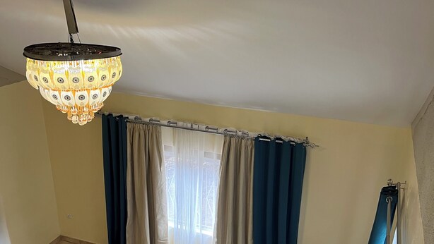 A living room with a grey sofa, a patterned chandelier, and a window with blue curtains.