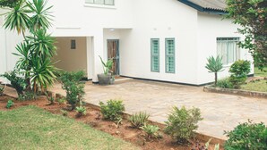 A white building with a tiled roof, a paved courtyard, and various plants.