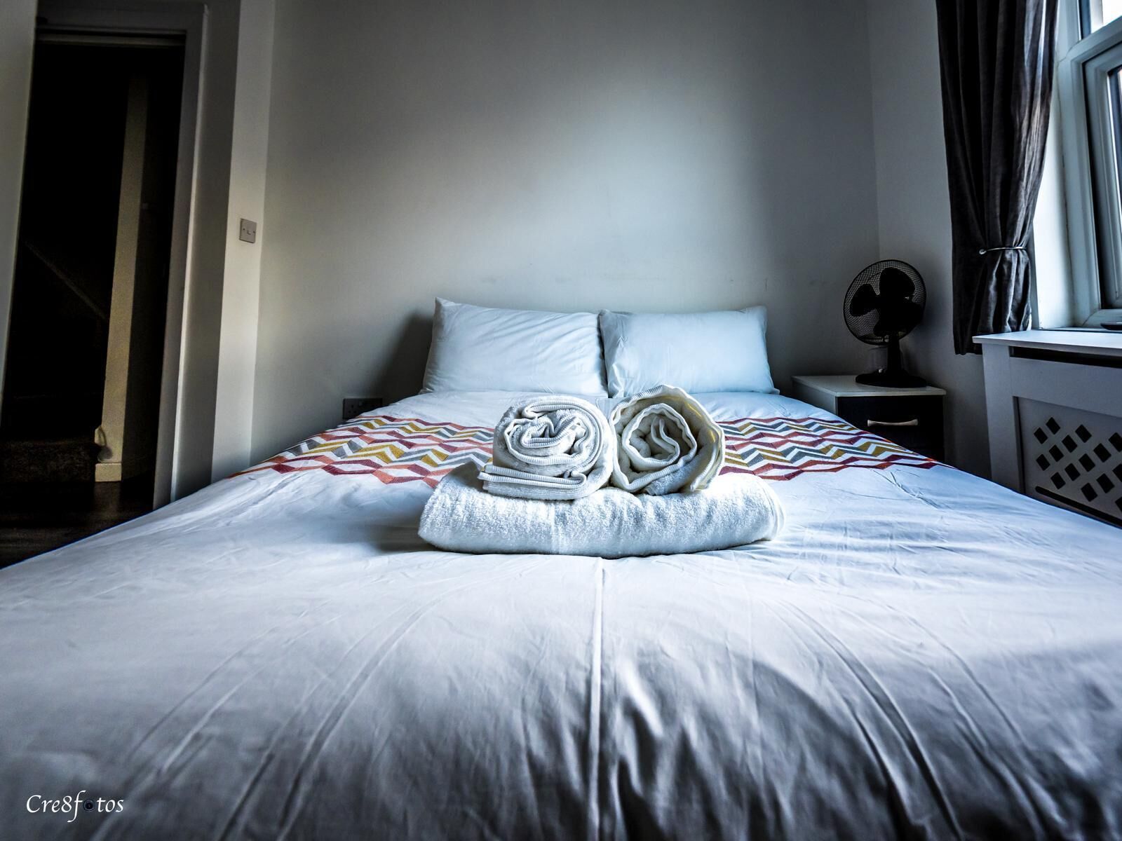 A neatly made bed with a folded towel and a patterned blanket.
