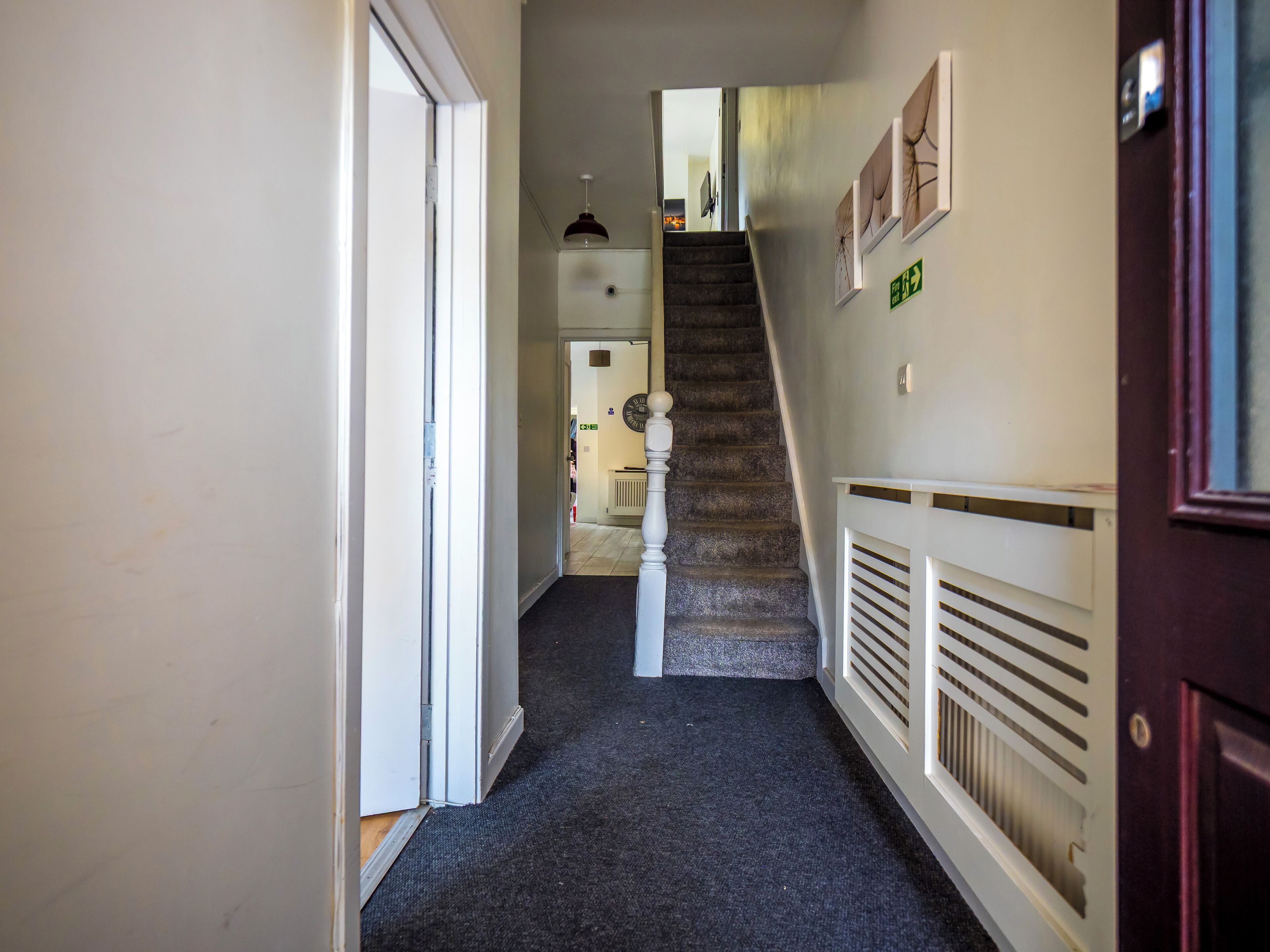 A hallway with a carpeted floor, a staircase with a white railing, and a door on the right.