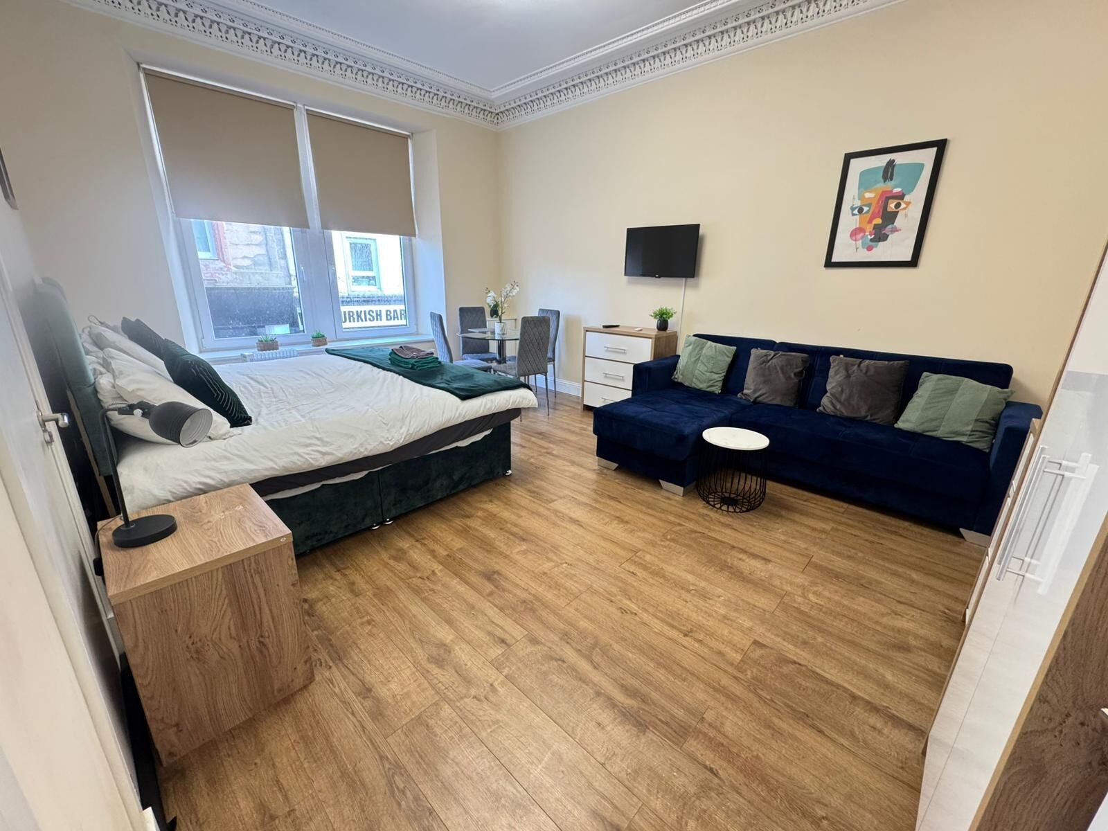 Ein Schlafzimmer mit einem Bett, einem blauen Sofa, einem kleinen runden Tisch und einem Fernseher an der Wand.