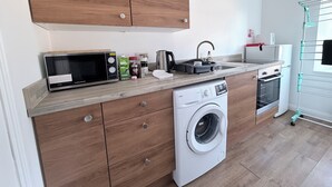 A modern kitchen with wooden cabinets, a built-in washing machine, a microwave, a kettle, and a sink. - Apartment 2- 216 High Street (Arbroath)