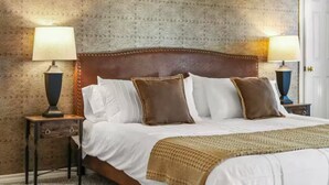 A neatly made bed with a brown headboard, white bedding, and a brown knitted throw. There are two bedside tables with lamps, and a patterned wallpaper on the wall. - 4BR Frisco Retreat Near Universal Kids Resort & Toyota + BBQ & Firepit (Frisco)