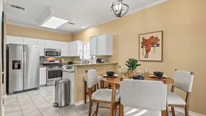 A modern kitchen with white cabinets, stainless steel appliances, and a dining area with a round table and four chairs. - 4BR Frisco Retreat Near Universal Kids Resort & Toyota + BBQ & Firepit (Frisco)