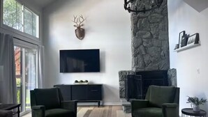 A modern living room with a stone fireplace, a mounted deer head, and a large flat-screen TV.