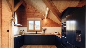 A modern kitchen with wooden beams, a black refrigerator, and a window with a view of a mountain. - Chalet Sheehy - Modern property with spa and terraces - OVO Network (La Toussuire)