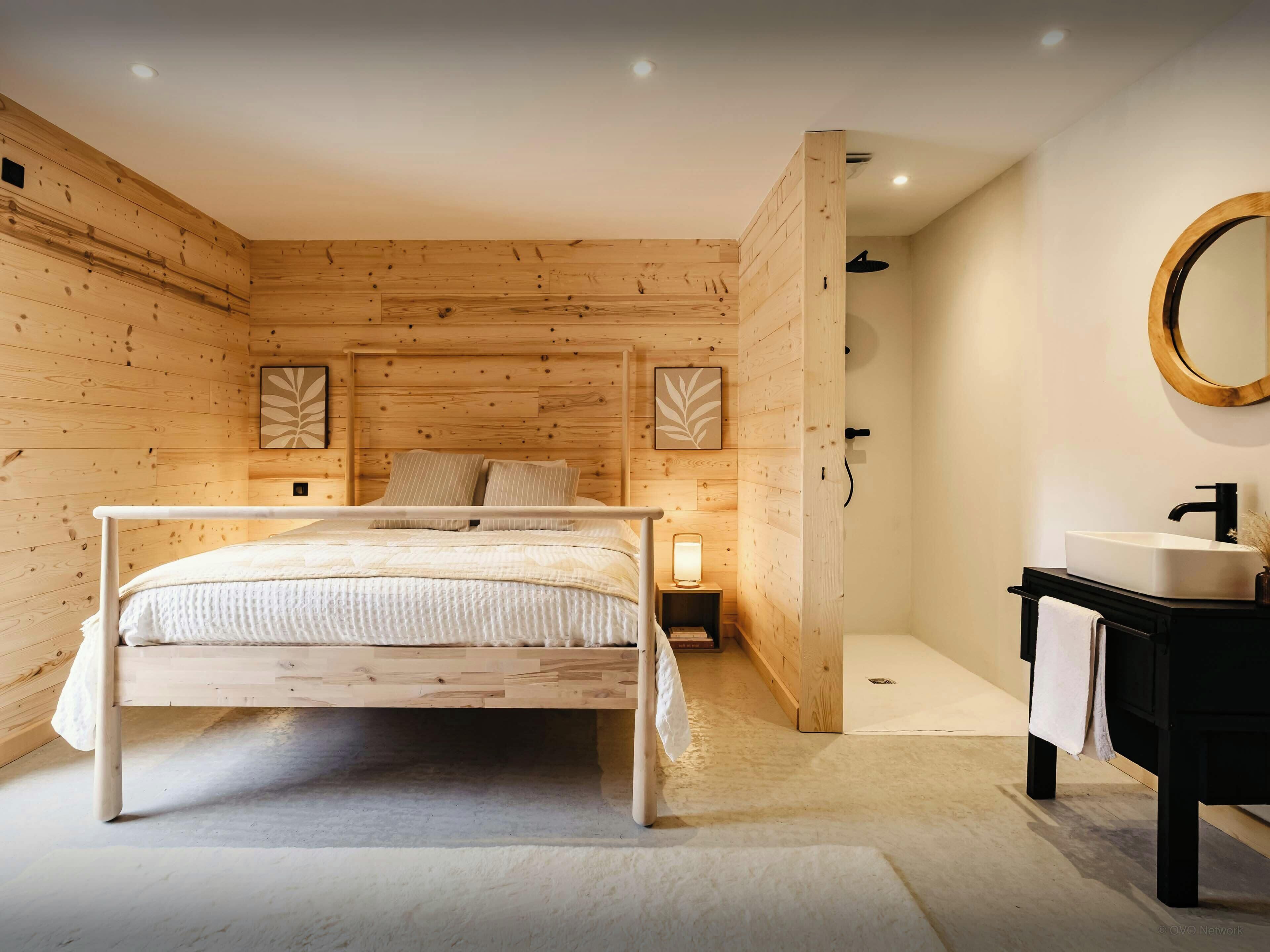 A bedroom with a wooden bed, bedside tables, a nightstand, a mirror, and a bathroom with a sink and towel rack.