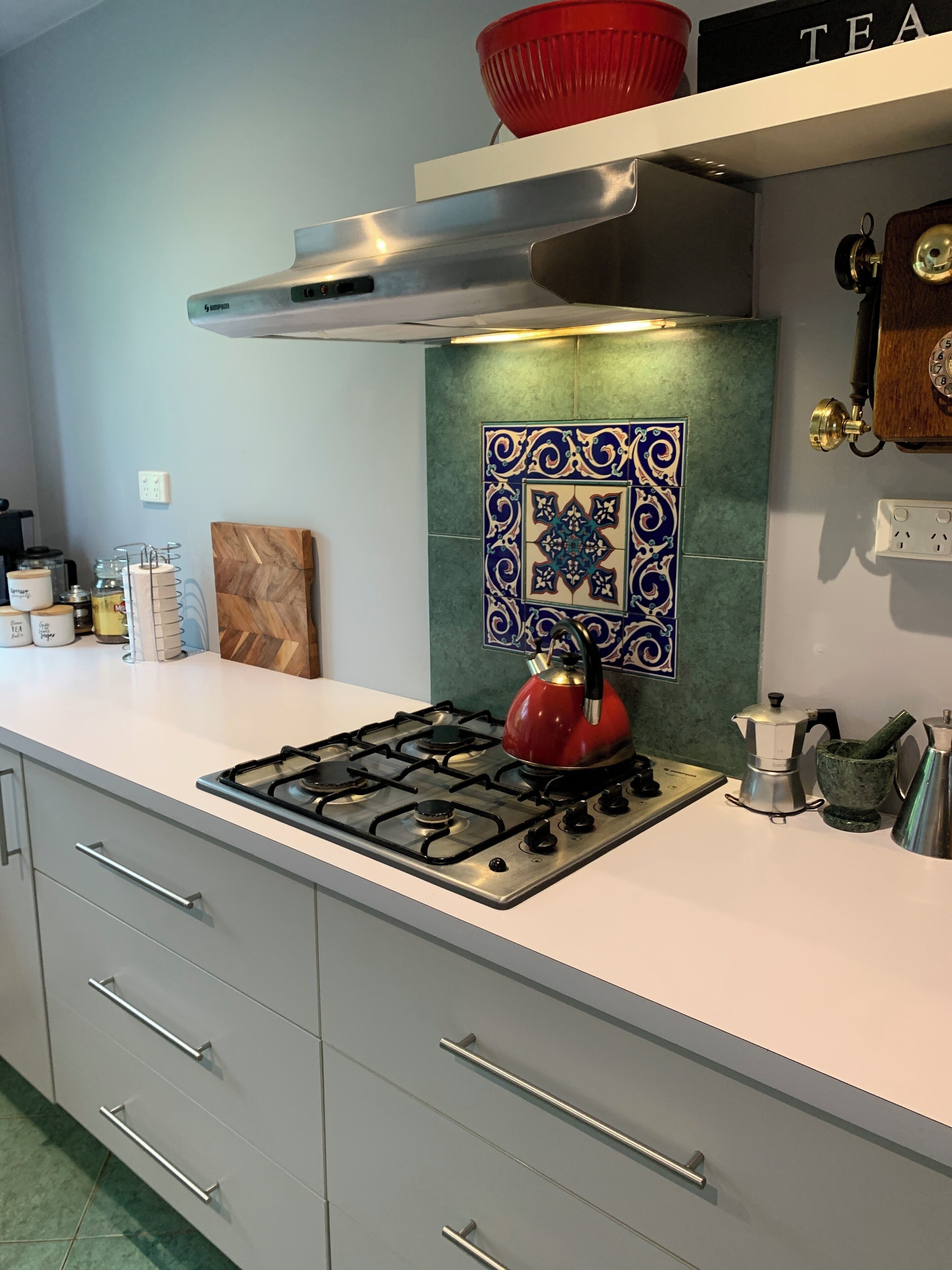 A modern kitchen with a gas stove, a red kettle, and a coffee maker.