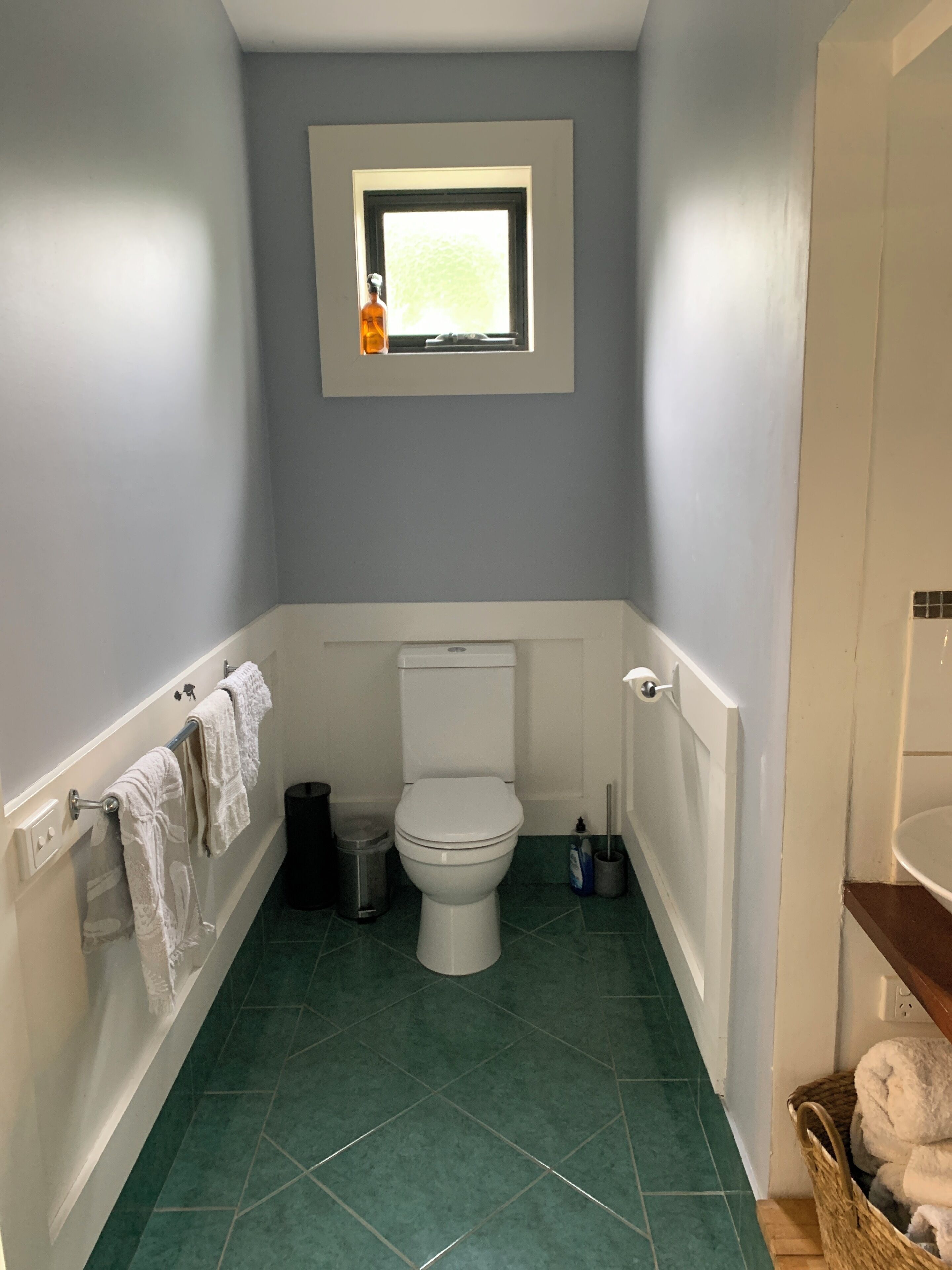A small bathroom with a toilet, a window, and a green tiled floor.