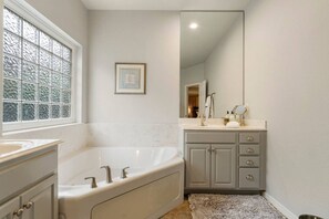 A bathroom with a bathtub, a vanity with a mirror, and a window with frosted glass.