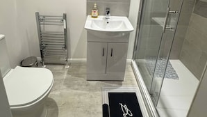 A modern bathroom with a white sink, a round mirror, a towel rack, and a glass-enclosed shower.