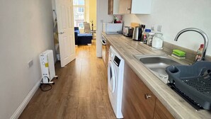 A compact kitchen with wooden flooring, a built-in washing machine, a sink, and a toaster.