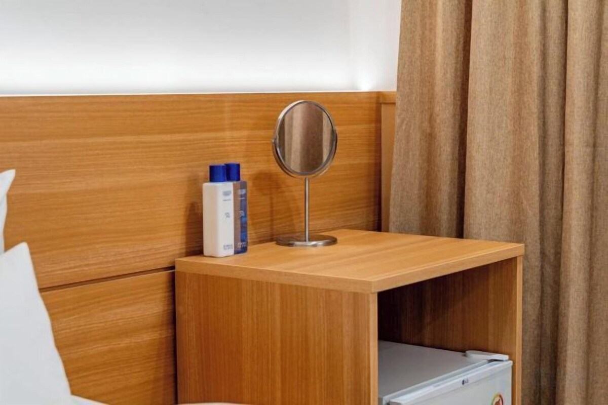 A wooden bedside table with a mirror, a bottle, and a small drawer.