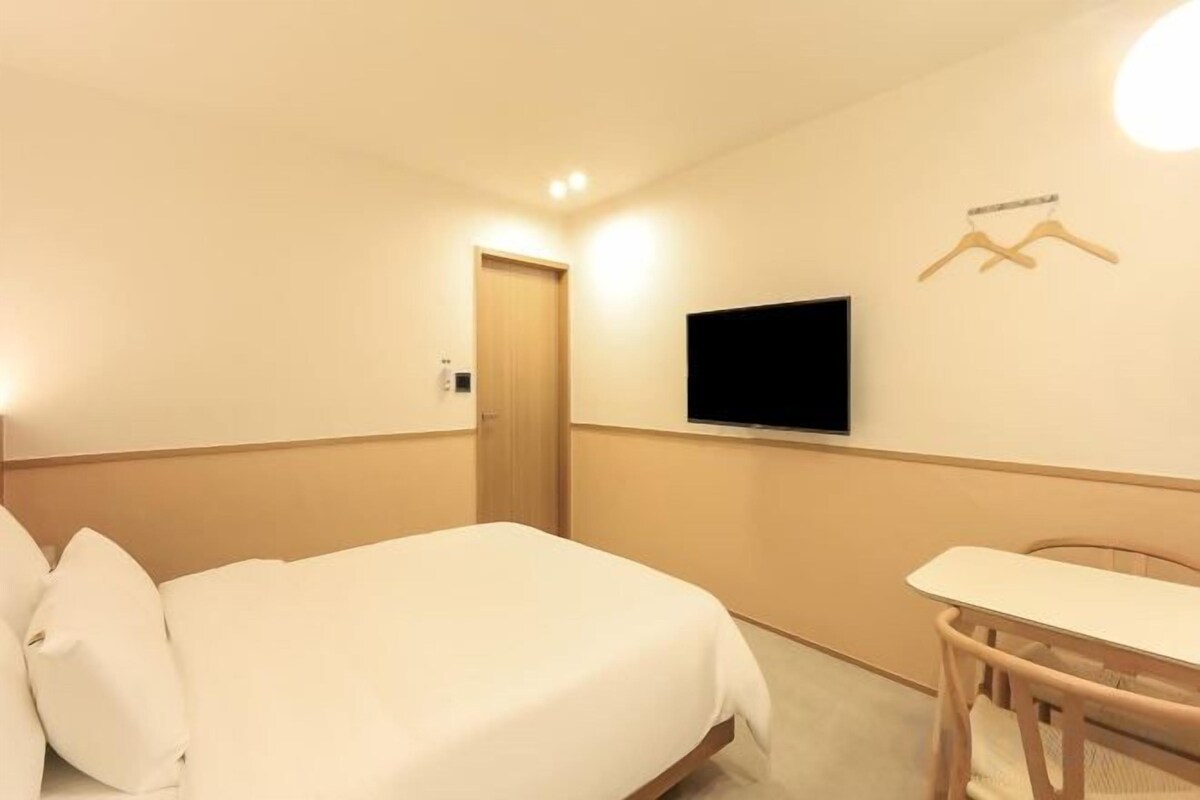 A hotel room with a bed, a television mounted on the wall, a desk, and a chair.