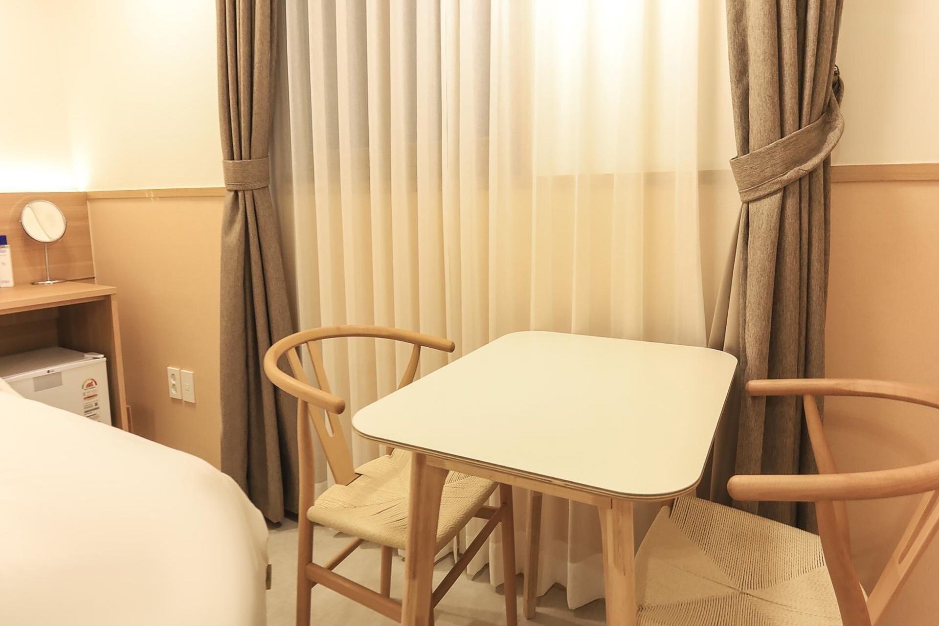 A hotel room with a bed, a small table, two chairs, and a mirror on a bedside table.