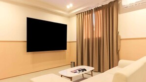 A hotel room with a flat-screen TV mounted on the wall, a white sofa, a small white table with a remote control, and a window with beige curtains. - Staylibera (Gangneung)