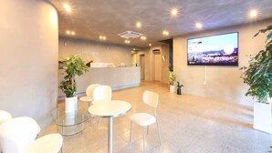 A reception area with a reception desk, chairs, potted plants, and a TV screen displaying a landscape. - Staylibera (Gangneung)
