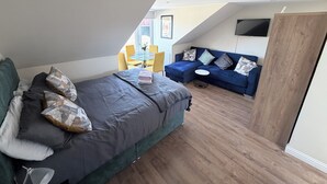 A modern loft bedroom with a large bed, a blue sofa, and a dining area with yellow chairs. - Apartment 6- 216 High Street (Arbroath)