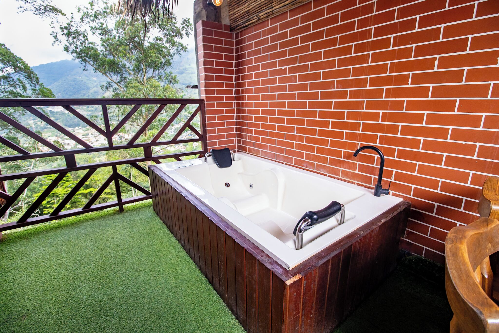 A wooden bathtub with a black faucet, a wooden chair, and a brick wall.