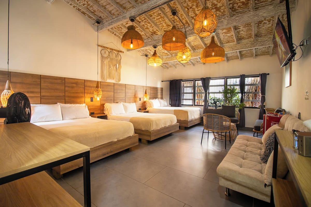 Een moderne hotelkamer met drie bedden, een houten tafel, rieten stoelen en een groot raam met uitzicht.