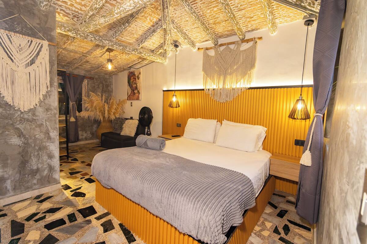 Een slaapkamer met een bed, een houten hoofdbord, macramé wanddecoraties en vloertegels met een patroon.