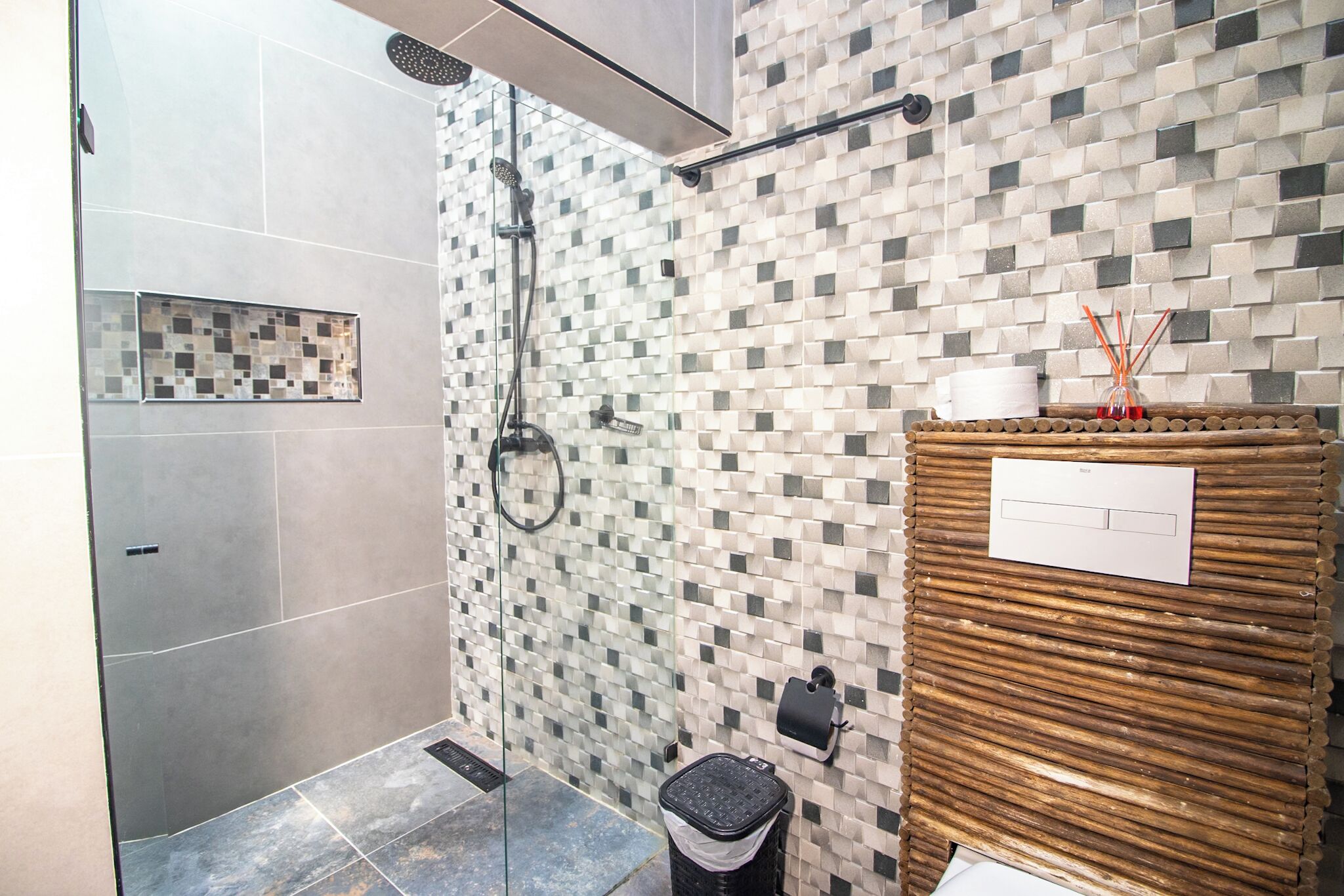 Une salle de bain moderne équipée d’une douche, de murs carrelés, d’une poubelle et d’un panneau en bois avec un porte-papier.