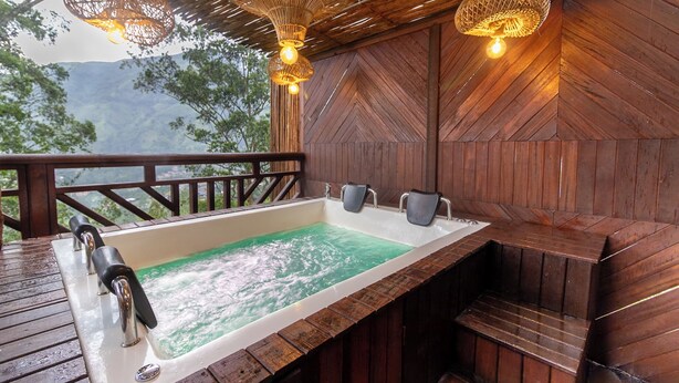 Een houten terras met een jacuzzi, omgeven door houten wanden en een rieten dak.