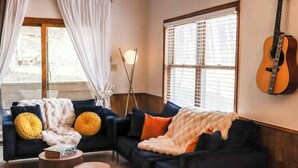 Ein Wohnzimmer mit einem dunkelblauen Sofa, einer weißen, flauschigen Decke und einer Gitarre an der Wand.