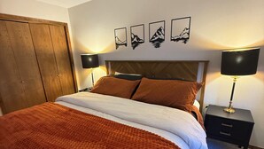 Ein Schlafzimmer mit einem Bett, einem Holzschrank, zwei Nachttischen mit Lampen und vier gerahmten Bildern an der Wand.
