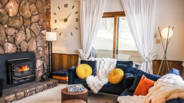 Ein gemütliches Wohnzimmer mit Kamin aus Stein, einer bequemen Sofagarnitur und einer großen Wanduhr.