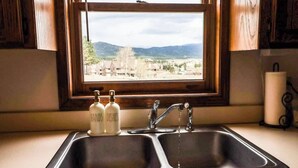 Eine Küche mit doppelter Spüle, Holzschränken und einem Fenster mit Blick auf eine Berglandschaft.