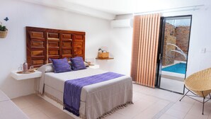 Une chambre avec un grand lit, une tête de lit en bois, une table de chevet avec une lampe, une petite étagère et une vue sur une piscine, visible à travers une porte-fenêtre coulissante.