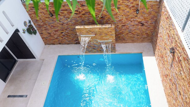 Une piscine rectangulaire à l’eau d’un bleu limpide, entourée d’un mur de briques et d’une structure blanche dotée d’une porte noire.