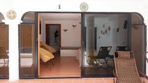 Une porte-fenêtre coulissante donne sur une pièce meublée de mobilier en osier et ornée de décorations murales.