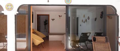 A sliding glass door leading to a room with wicker furniture and decorative wall hangings.