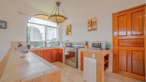 A kitchen with wooden cabinets, a stove, a microwave, and a large window. - Oasis 17 - Group Getaway (La Fortuna)