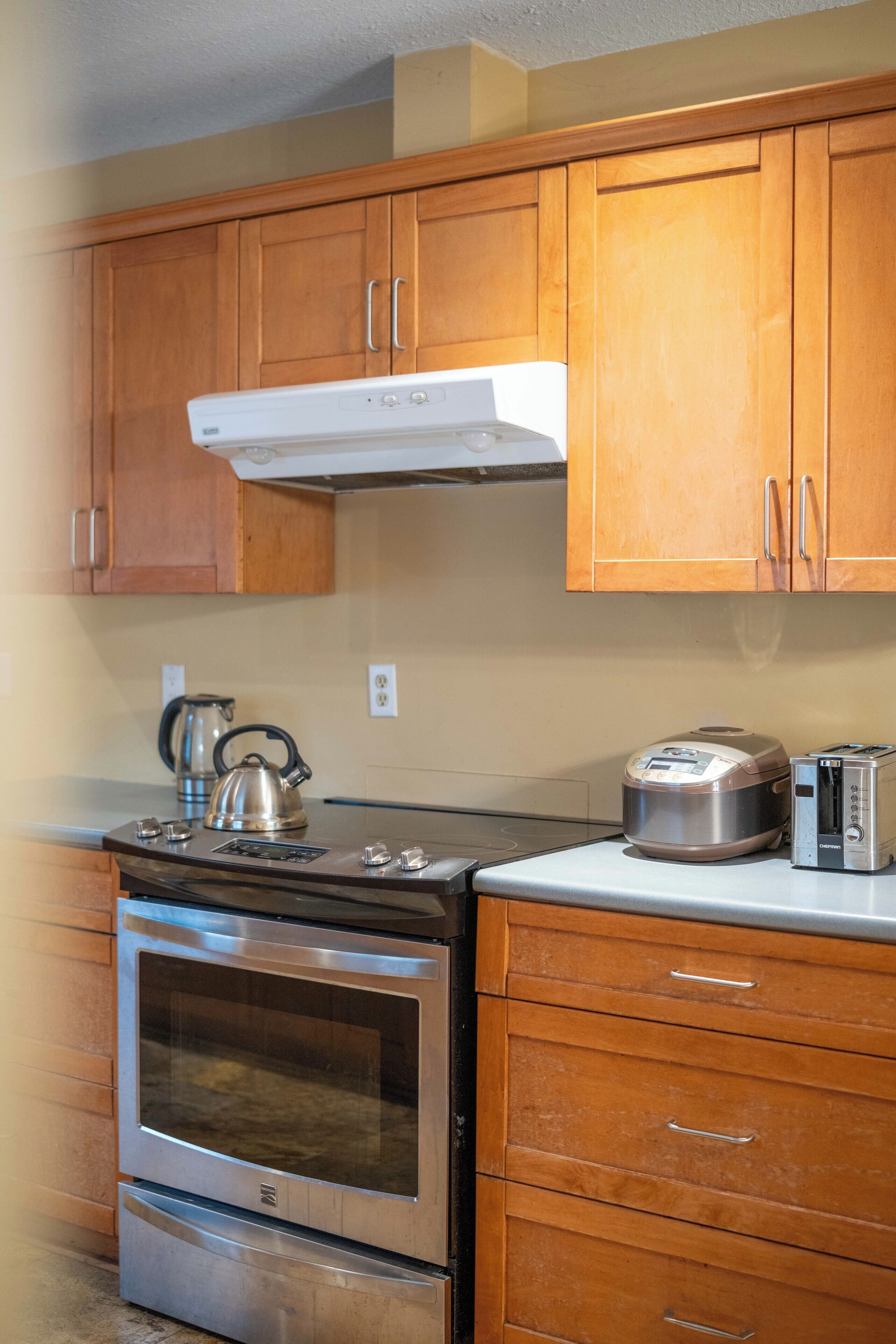 A kitchen with wooden cabinets, a stainless steel oven, a kettle, and a toaster.