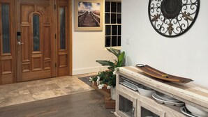 Ein Korridor mit Holztüren, einem gerahmten Gemälde, einem dekorativen Metallwandkunstwerk und einem Holzschrank mit Geschirr.