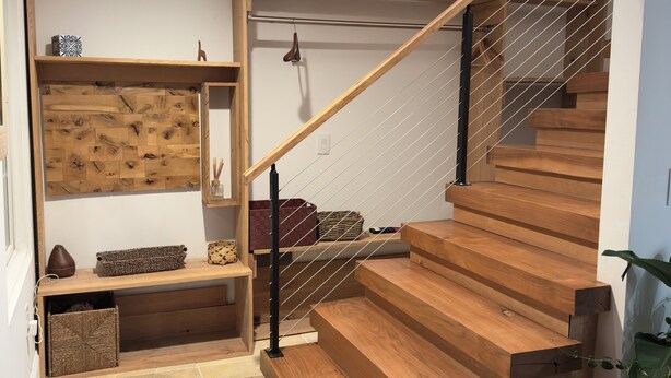Eine moderne Treppe mit Holzstufen und einem schwarzen Geländer, die zu einem Erkerbereich mit Oberlicht führt.
