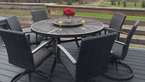 Eine runde Holzdielen-Terrasse mit Korbstühlen und einem Tisch, mit Blick auf eine malerische Landschaft aus Bäumen und Bergen.