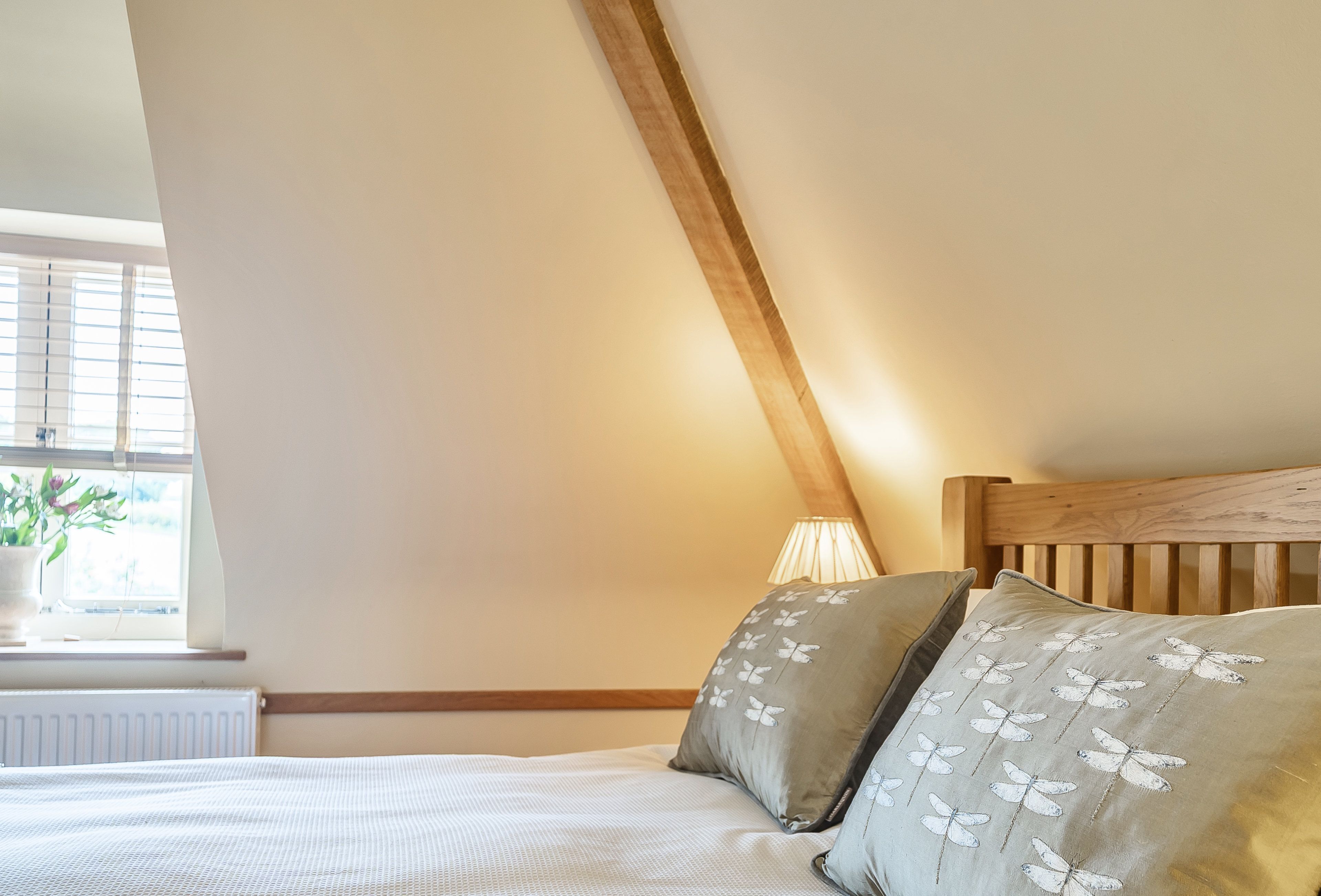 A bedroom with a sloped ceiling, a wooden headboard, and a window with a plant.