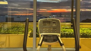A stationary exercise bike with a digital display, positioned in front of a window overlooking a cityscape at sunset. - KanStay Sea View Condo by Manila Bay｜康宿·海境居 (Manila)
