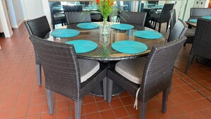 A round dining table with black wicker chairs, teal placemats, and a vase with flowers. - Relaxing Beachfront Oceanview Condo w/2 Beds 2 Full Baths, Kitchen, Pet Friendly (Galveston)