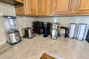 A kitchen with a blender, toaster, coffee maker, and coffee containers on the counter.