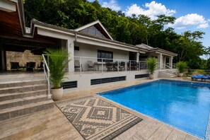 A modern house with a swimming pool, outdoor seating, and a staircase leading to a covered patio.