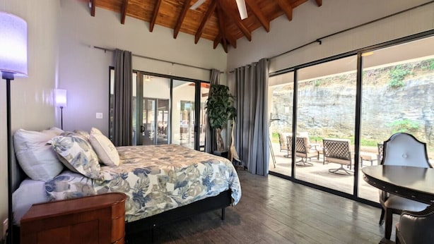 Een slaapkamer met een groot bed, een houten plafond en uitzicht op een terras.