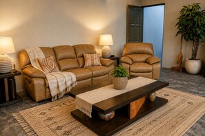 A living room with a brown leather sofa, a matching armchair, a coffee table, and a potted plant.
