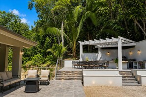 An outdoor patio with a pergola, seating area, and a barbecue setup.