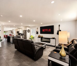 Un salon moderne avec un canapé en cuir noir, une table basse et un téléviseur fixé au mur qui affiche « NETFLIX ».