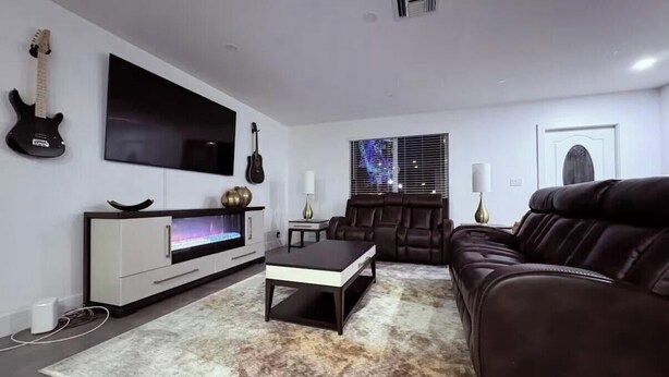 A living room with a TV, a sofa, a coffee table, and a guitar. - 3BR Guitar House + Poker Lounge Near Hard Rock (Hollywood)